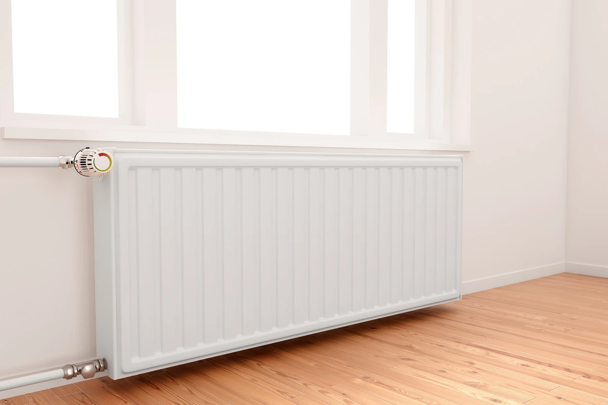 Intérieur résidentiel avec radiateur à panneaux blanc installé sous fenêtre, sol en parquet bois clair, murs blancs