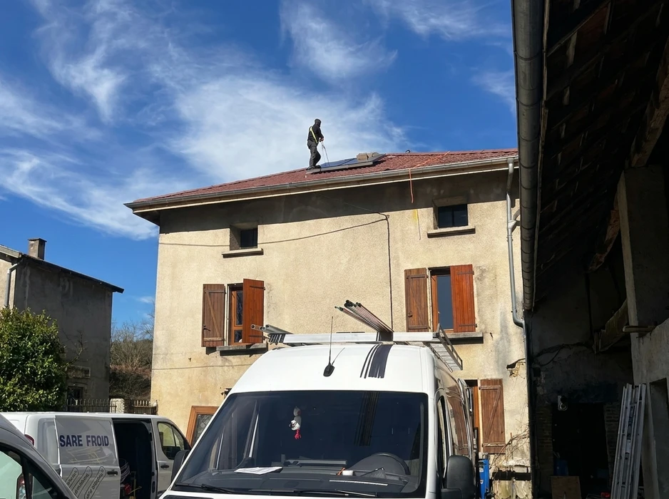 Technicien en combinaison noire sur toiture en tuiles rouges, installant des panneaux photovoltaïques