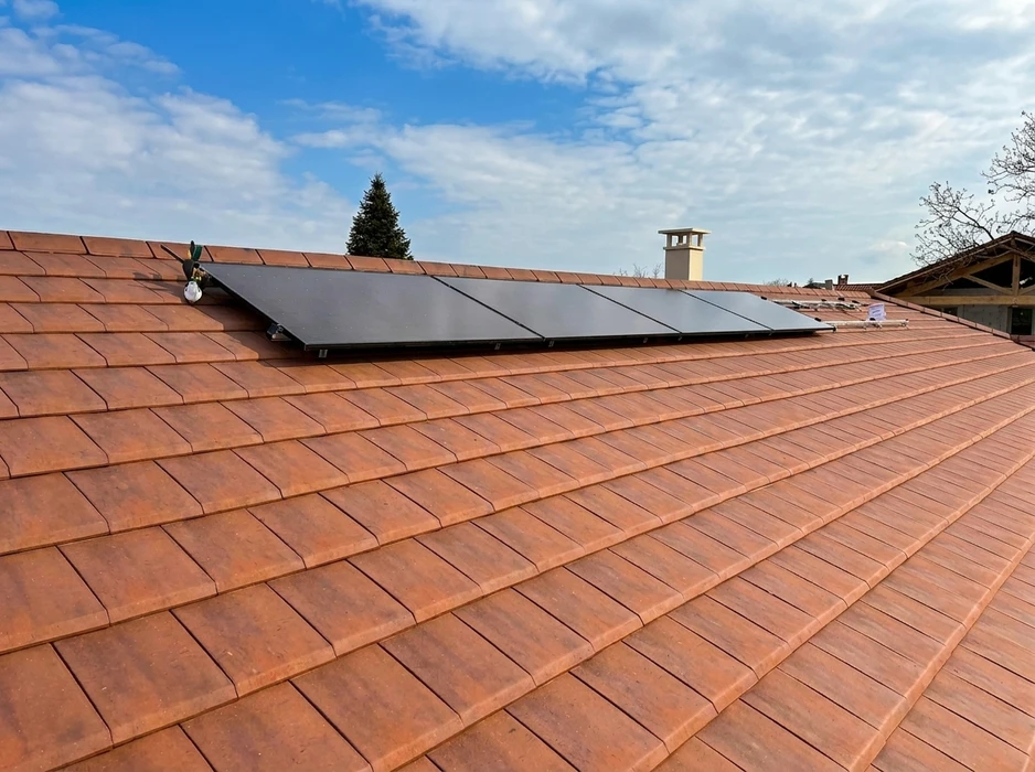 Toiture en tuiles canal terre cuite rouge-orangé, avec une rangée de 5 panneaux solaires photovoltaïques monocristallins noirs installés en portrait sur la rive de faîtage