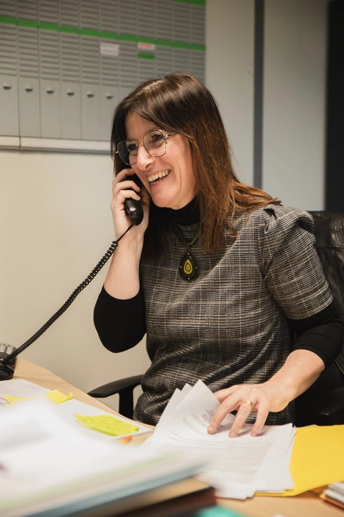 Photographie d'un artisan qualifié RGE assis à son bureau, en train de revérifier ou de signer un dossier administratif complet d'aide financière, avec un sourire professionnel et assuré. Au arrière-plan discret, on peut apercevoir des certifications ou qualifications affichées. L'image doit transmettre la confiance, la compétence administrative et l'expertise d'un professionnel maîtrisant les dossiers de subventions.