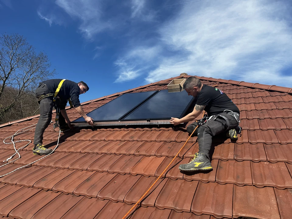 Installation de chauffe-eau solaire sur toiture métallique résidentielle sous ciel bleu nuageux