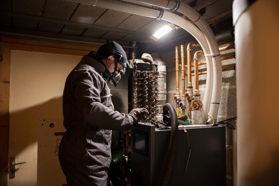 Un technicien en chemise à carreaux ajuste les paramètres d'une chaudière murale domestique tout en consultant un carnet de maintenance