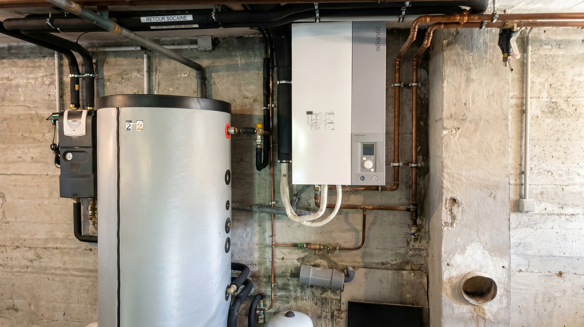 Un technicien en combinaison bleue effectue la maintenance d'une chaudière murale domestique
